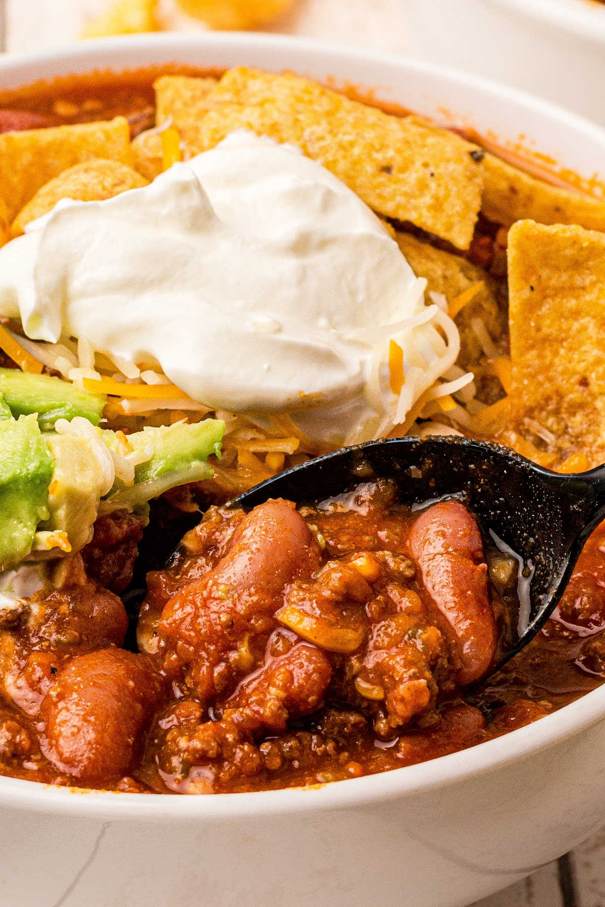 close up of a bowl of venison chili with beans, sour cream, avocado and corn chips