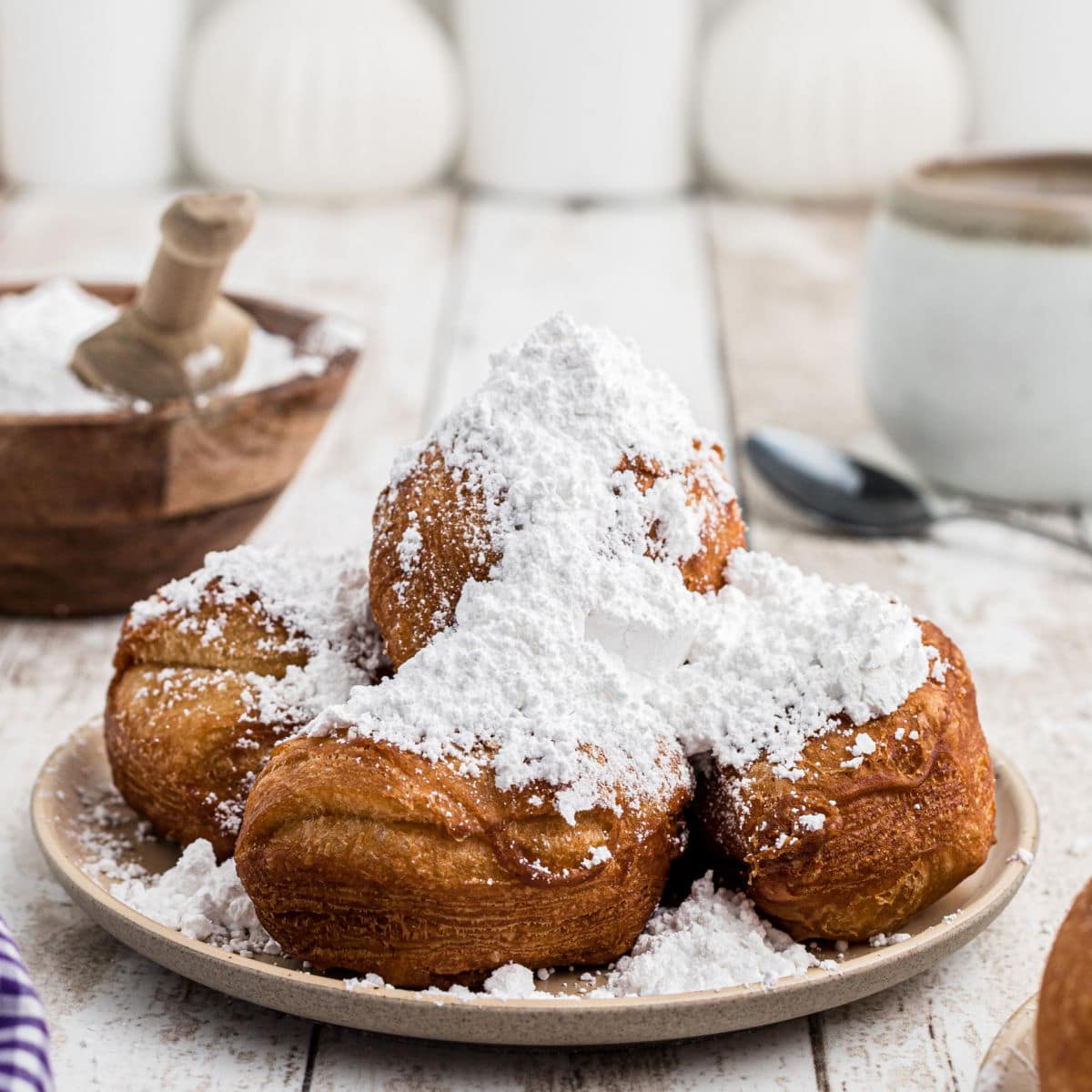 a close up image of biscuit beignets on a plate heaped high with powdered sugar
