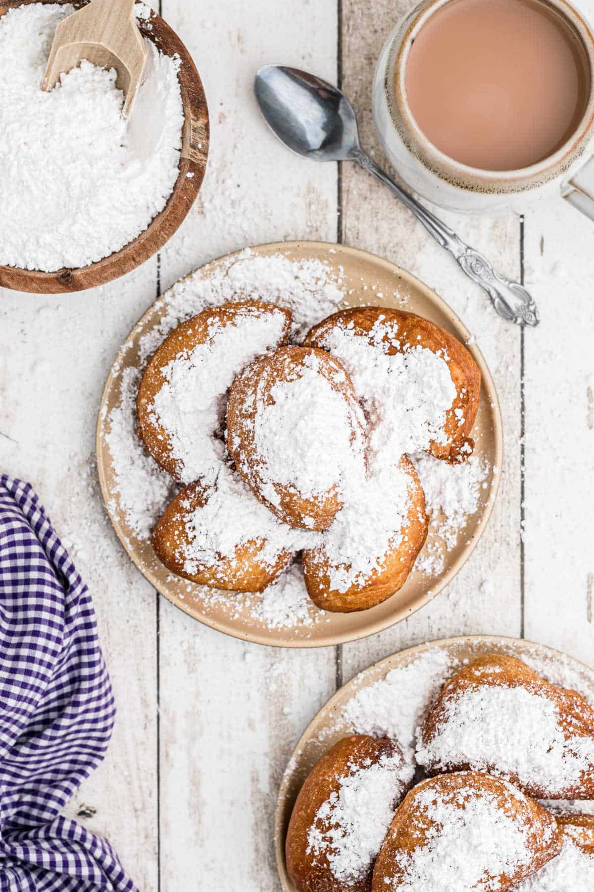 overhead shot of some biscuit beignets on a plate with a coffee on the side and a bowl of powdered sugar