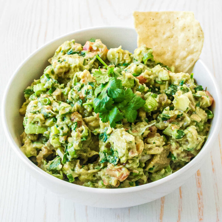 a bowl full of guacamole with tomatoes and a sprig of cilantro on top with a chip hanging out