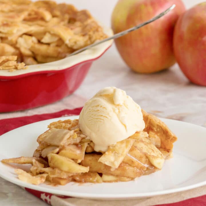 a slice of country apple pie dished out on a plate with a scoop of ice cream on top