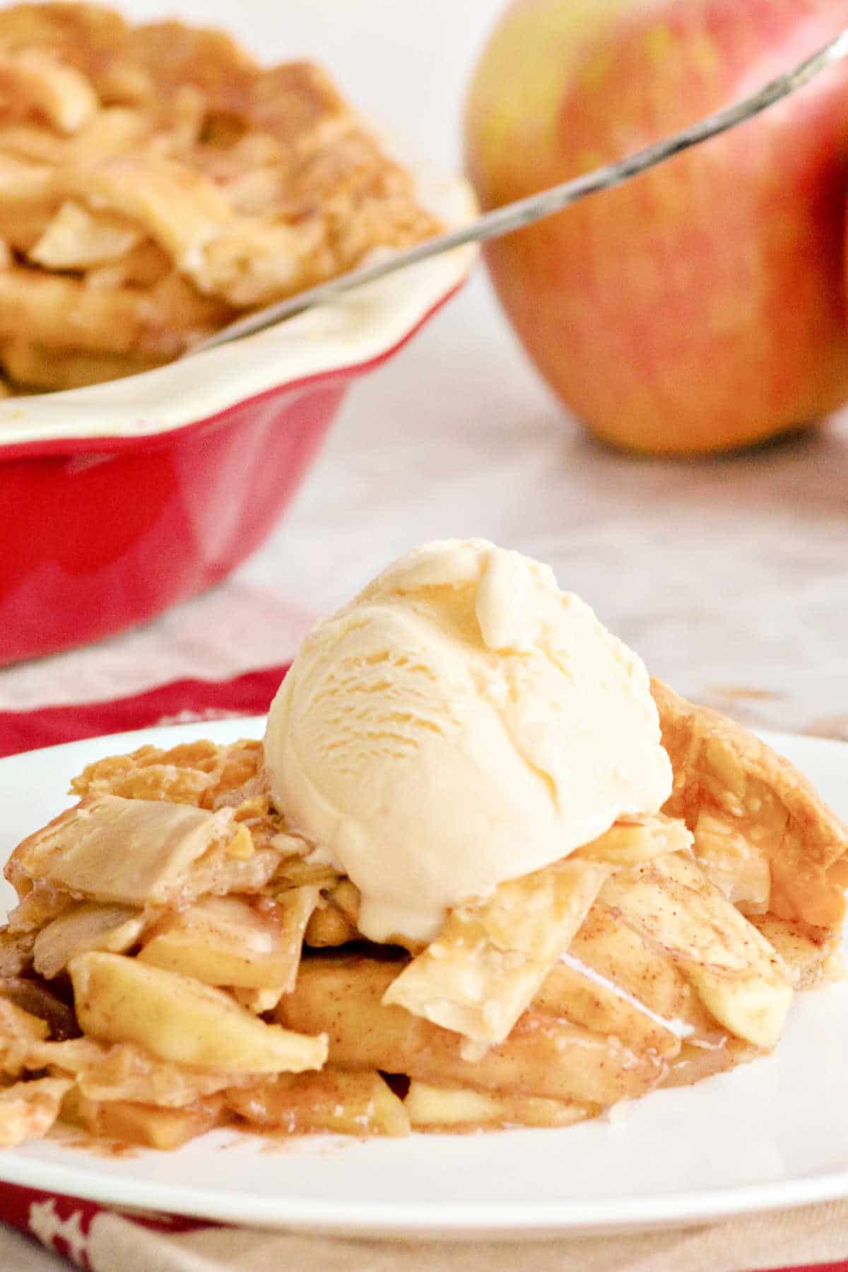 a slice of country apple pie dished out on a plate with a scoop of ice cream on top