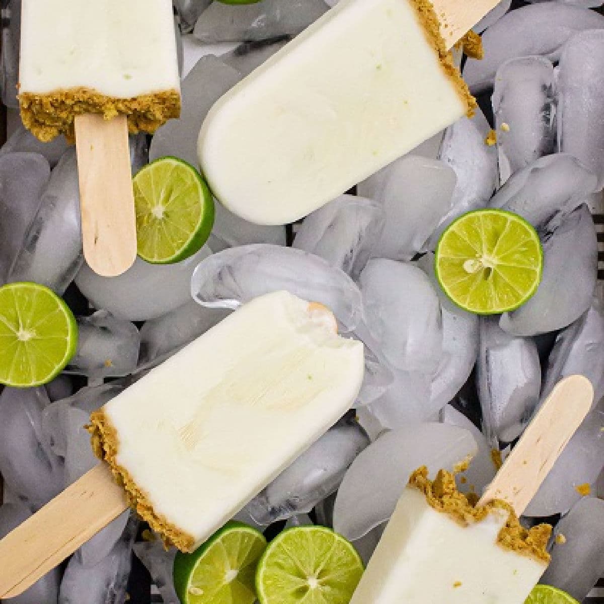 key lime pie popsicles laying on top of ice with slices of limes scattered around and one with a bite taken out of it