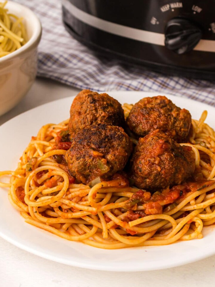 close up of a plate of spaghetti and meatballs with a crock pot in the background