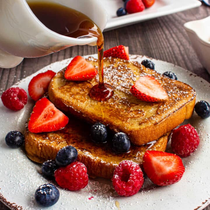 plate of french toast with fresh fruit and sugar with syrup being poured on top