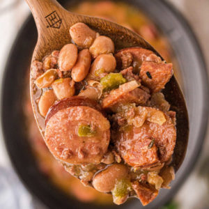 Close up of some pinto beans and sausage on a spoon over a crock pot.