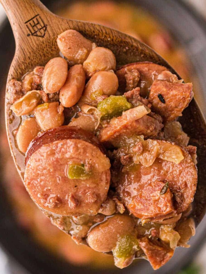 Close up of some pinto beans and sausage on a spoon over a crock pot.