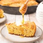 a piece of cornbread with a slice of butter on top and honey being poured over the top
