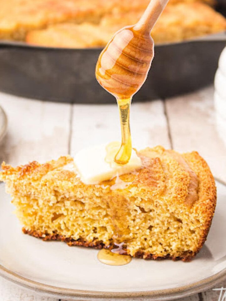 a piece of cornbread with a slice of butter on top and honey being poured over the top