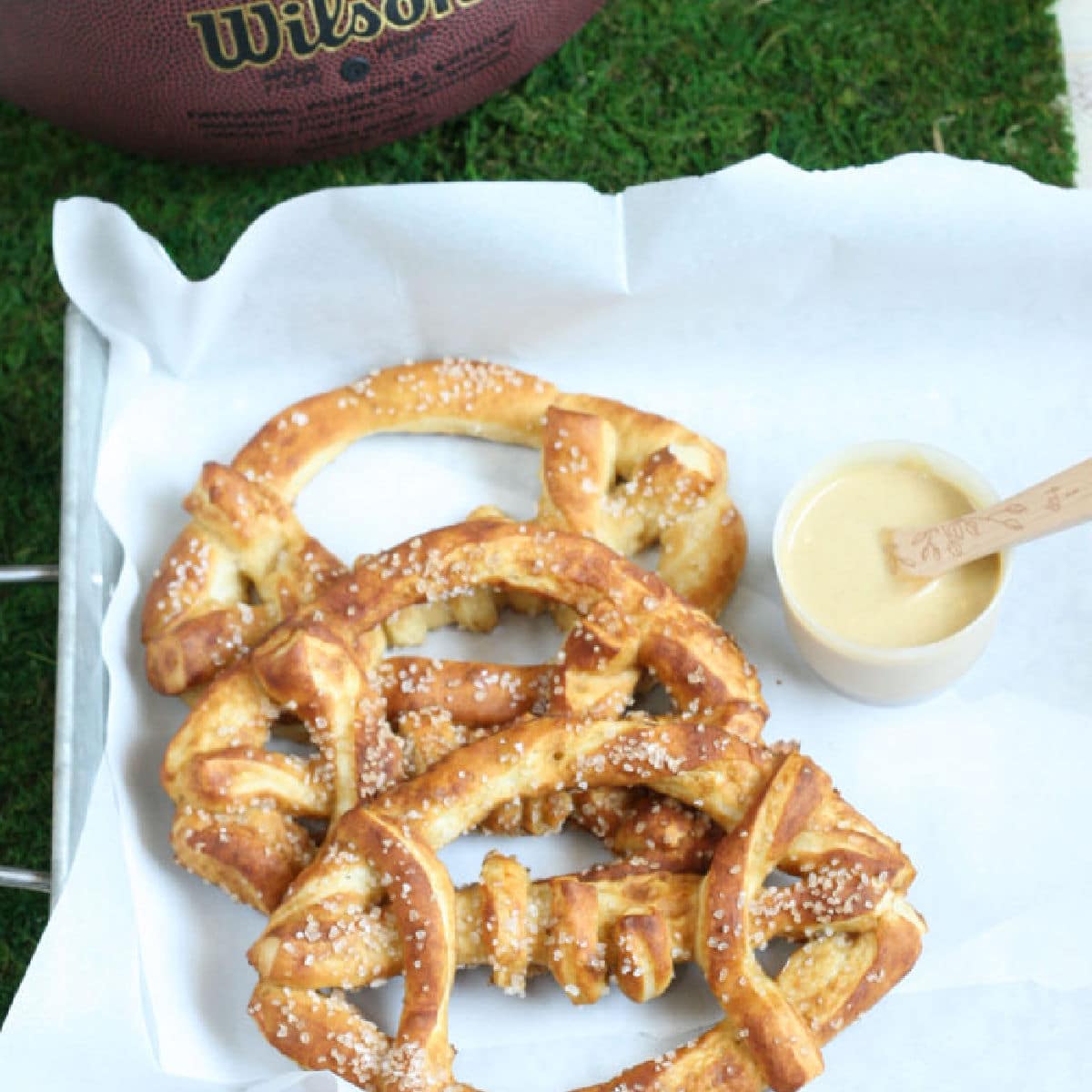 3 football shaped pretzels on a platter with a dip next to it