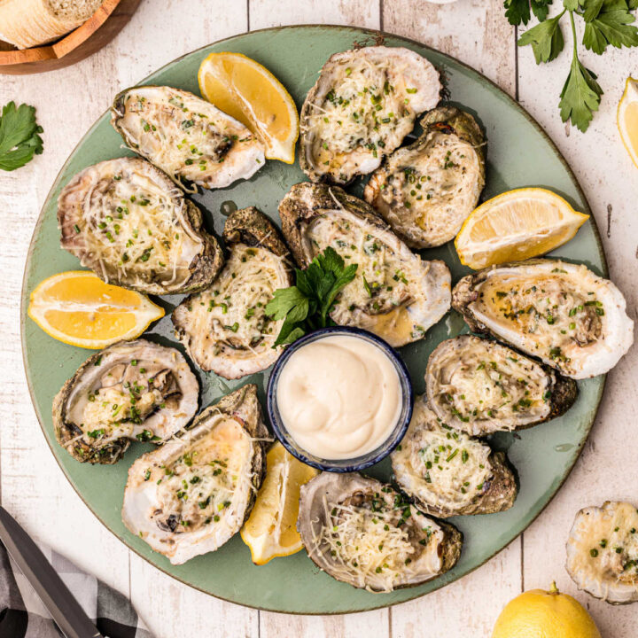a round plate full of chargrilled oysters with lemon wedges and dips