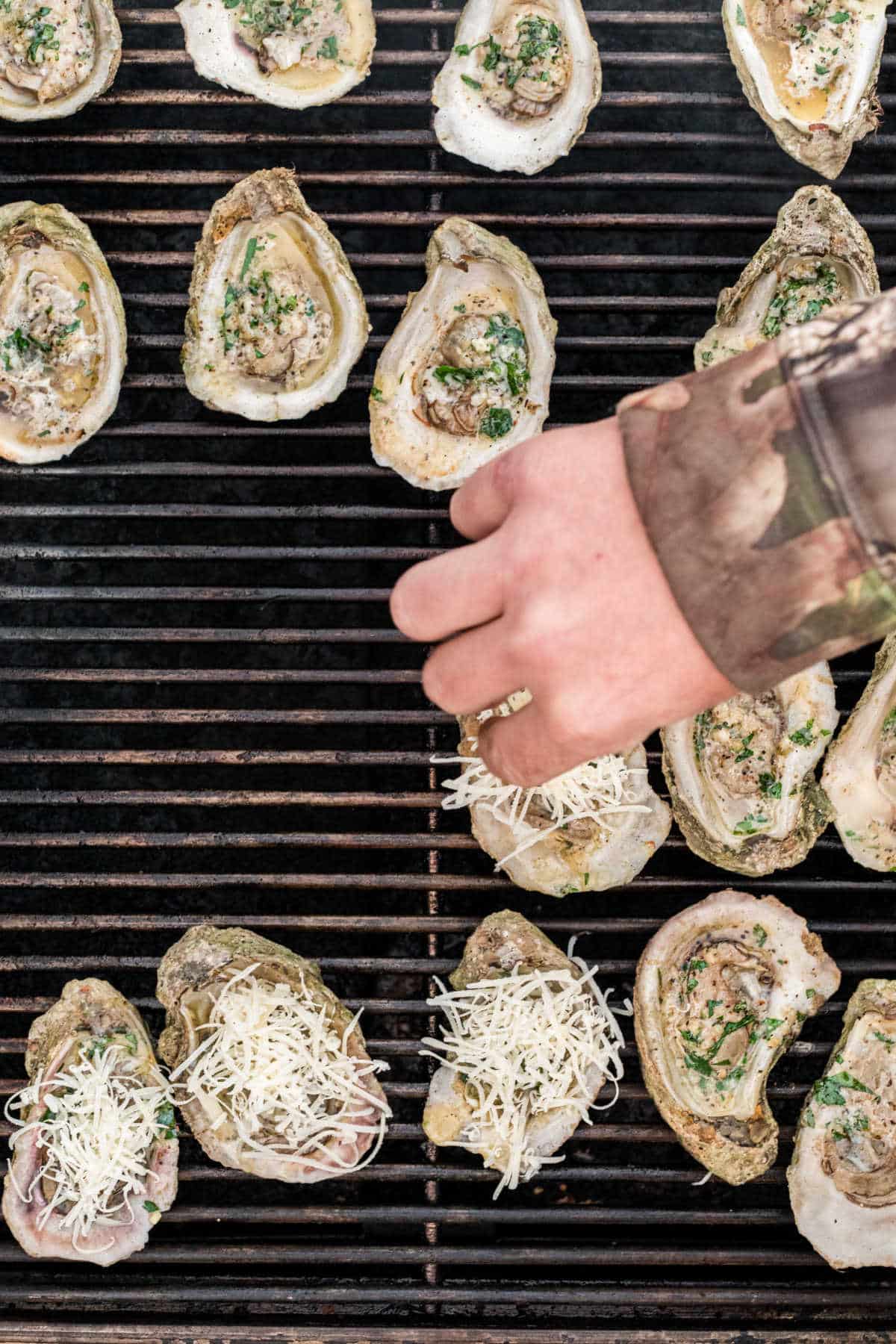 oysters on the half shell on the grill with parmesan cheese being sprinkled on top