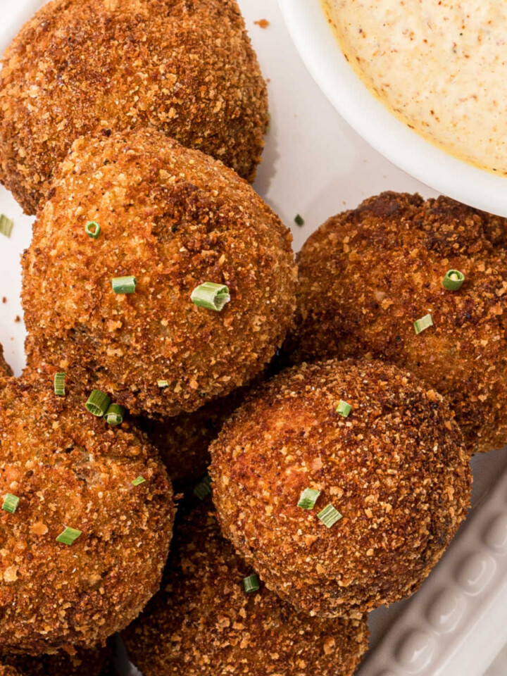 Close up of boudin balls with a hint of the mustard cream sauce peeking in, sprinkled with green onions on top.