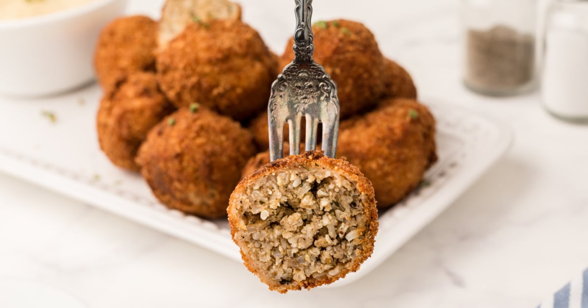 half of a boudin ball on a fork with boudin balls in the back ground