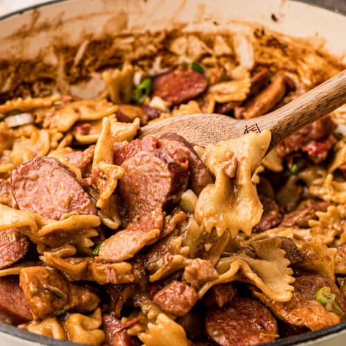 Close up of a pot of pastalaya with bow tie noodles and sausages with a spoon digging in