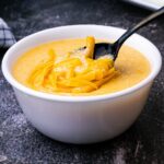 a bowl of cheese grits with grated cheese melting on top with a spoon diving in