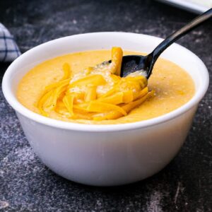 a bowl of cheese grits with grated cheese melting on top with a spoon diving in
