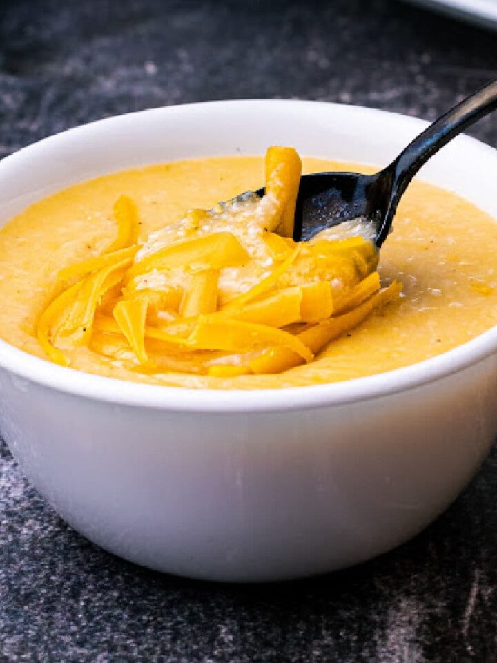 a bowl of cheese grits with grated cheese melting on top with a spoon diving in