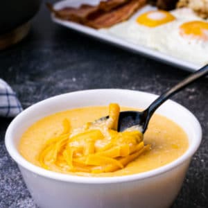 close up of cheese grits in a bowl with a spoon digging in