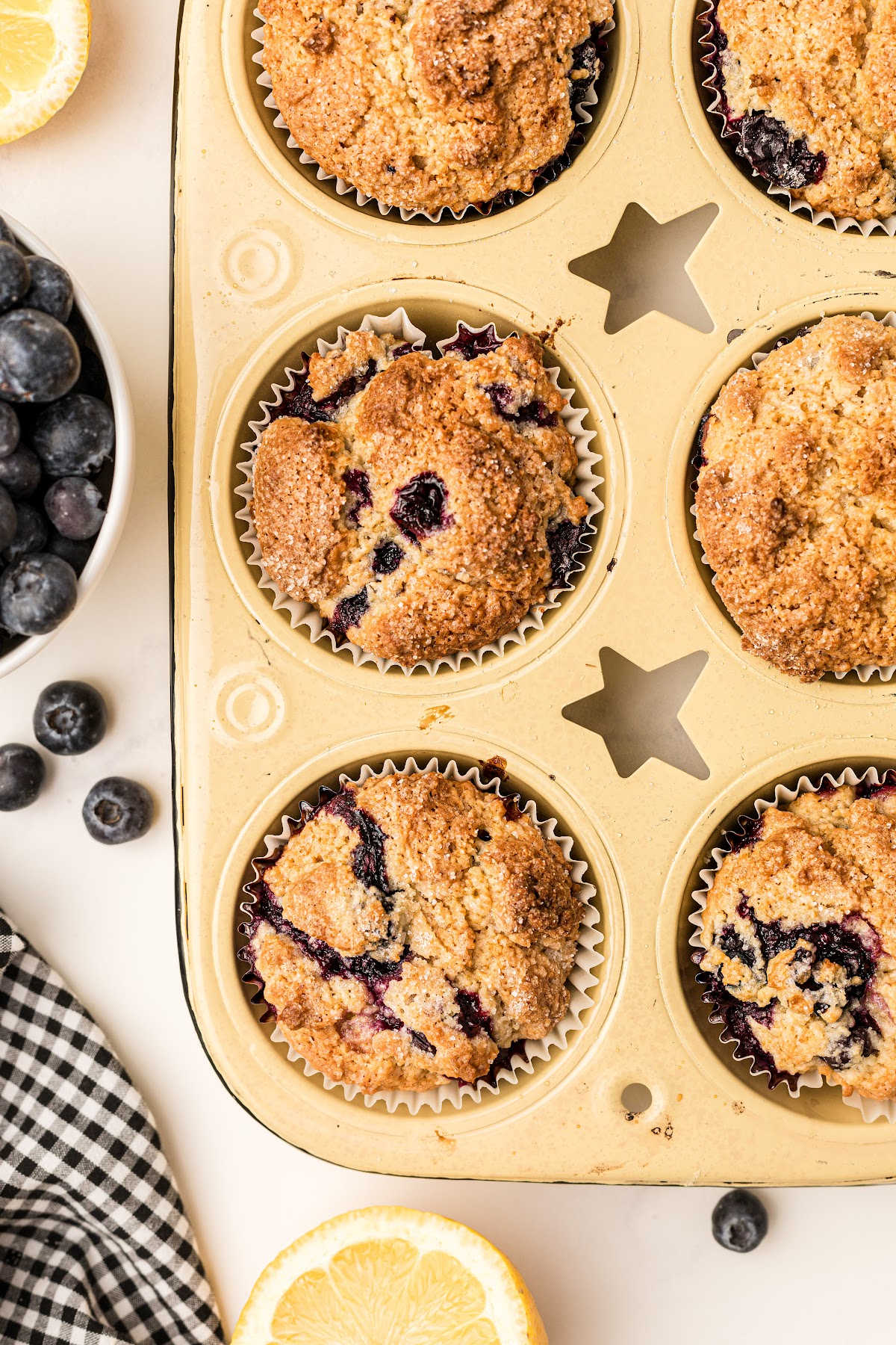 a yellow muffin tin with lemon blueberry muffins cooked in it
