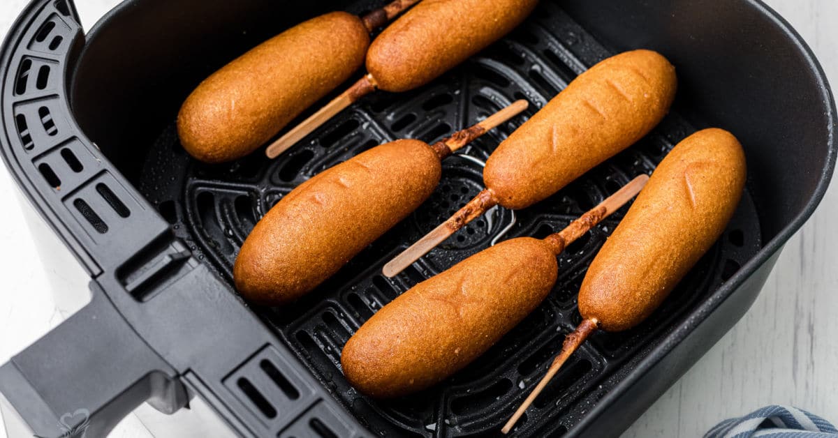 plate of corn dogs stacked up with one having a bite taken out of it on the top