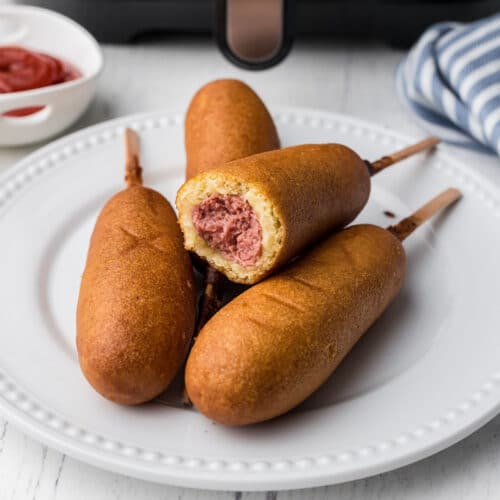 air fryer corn dogs in a pile on a plate in front of an air fryer featured image