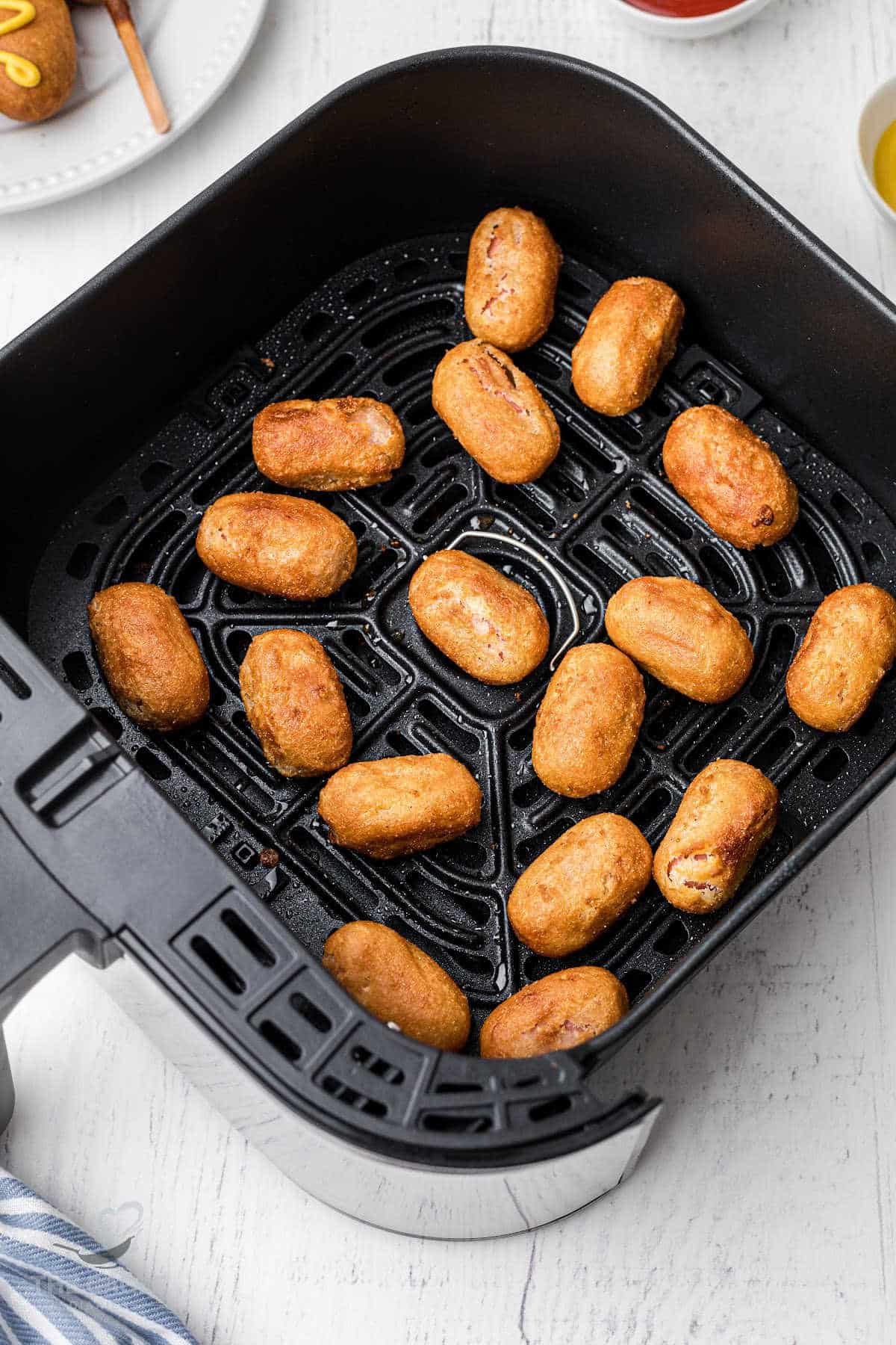 mini corn dogs laid out in a basket of an air fryer
