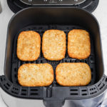 an air fryer basket with 5 hash brown patties lined up