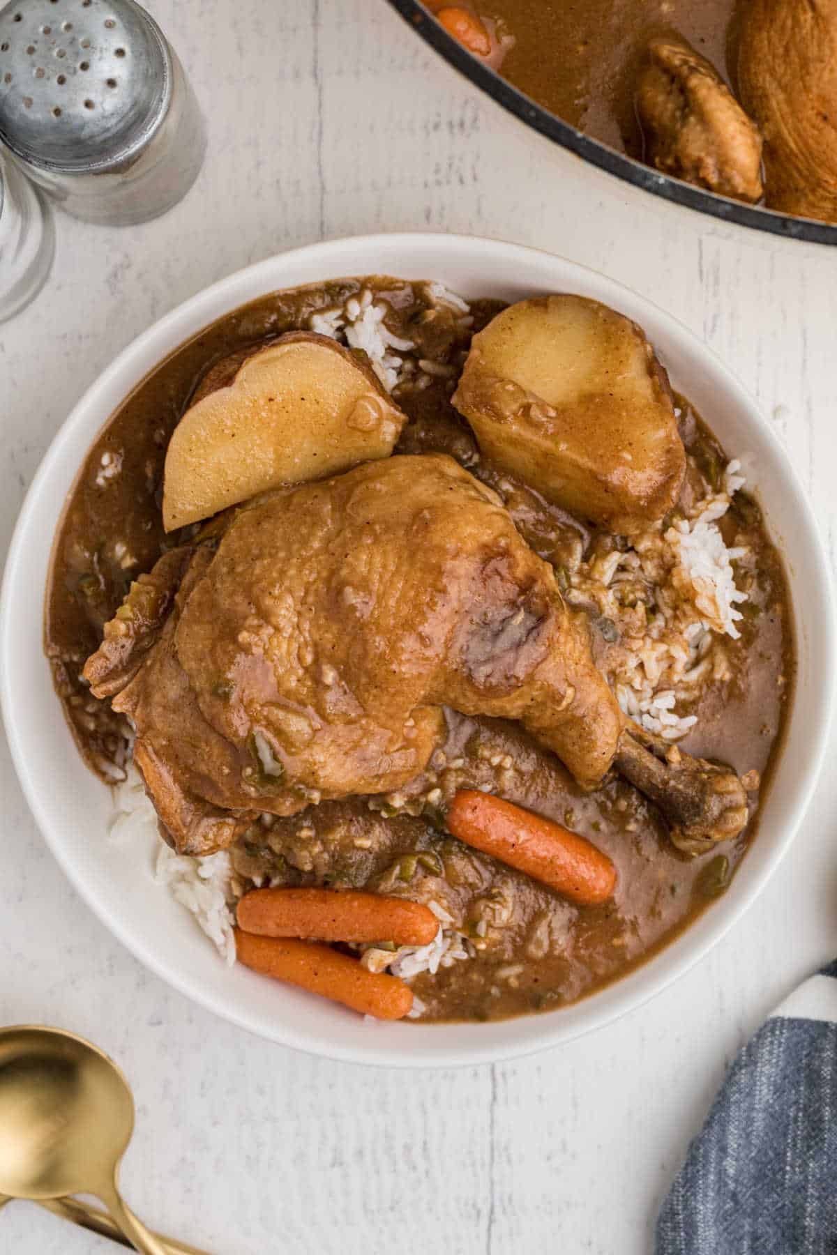 bowl of rice topped with chicken stew, whole leg with carrots and potatoes