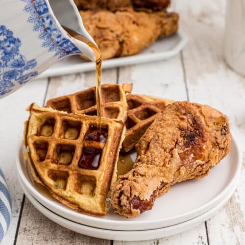 plate of fried chicken with waffles on the side with syrup being poured over the top