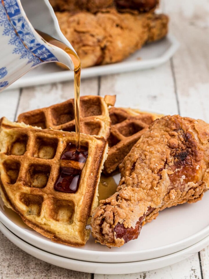 plate of fried chicken with waffles on the side with syrup being poured over the top
