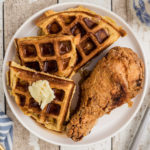 plate with a fried chicken drumstick and a side of waffles with syrup and butter