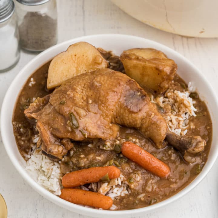 bowl of rice topped with chicken stew, whole leg with carrots and potatoes