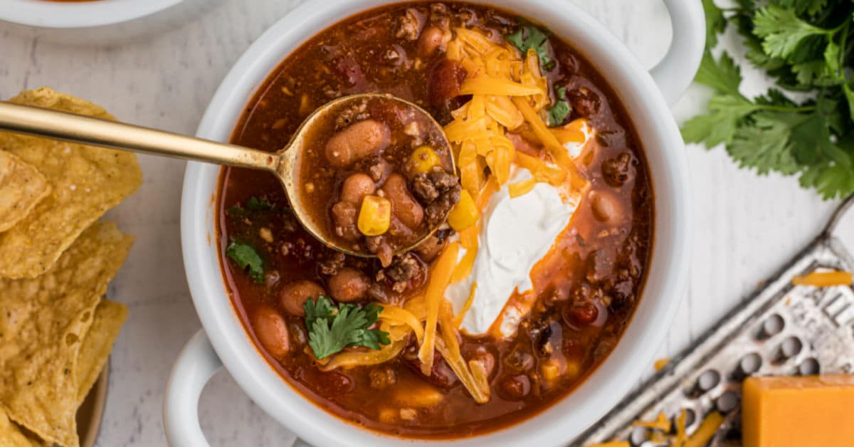 close up of a bowl of taco soup with grated cheese and sour cream with a spoon digging in