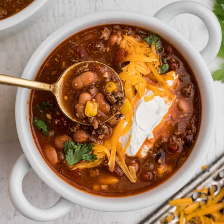 bowl of taco soup with grated cheese and sour cream with a spoon digging in