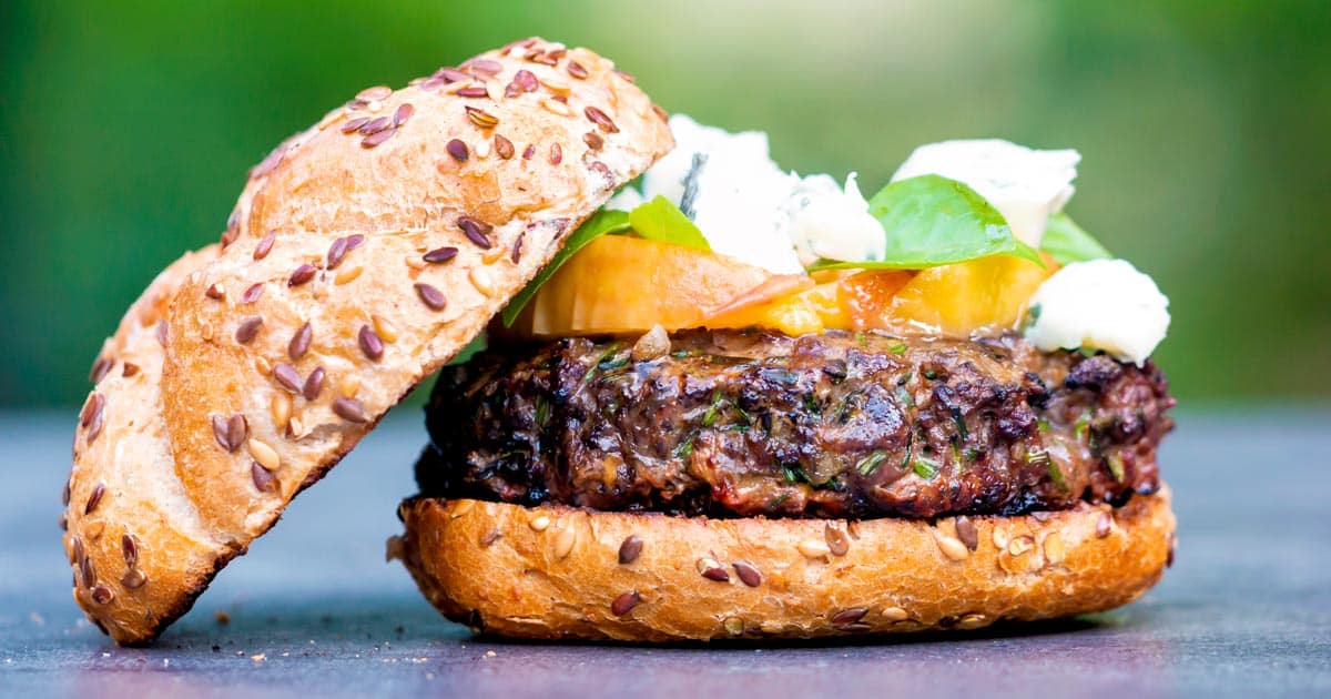 a delicious hamburger made from venison meat with peaches on top with a seeded bun