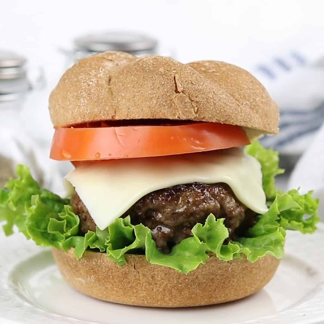 a tall burger with lettuce on the bottom a venison burger sitting on top with a slice of cheese and tomato, inside a bun