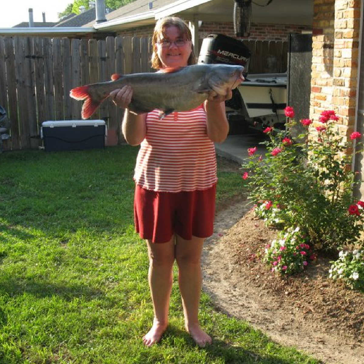 A picture of Melanie Cagle\'s mom, holding a large catfish, in the backyard.