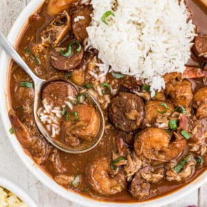 Close up of a bowl of seafood gumbo with a pile of rice and a spoon digging into it.
