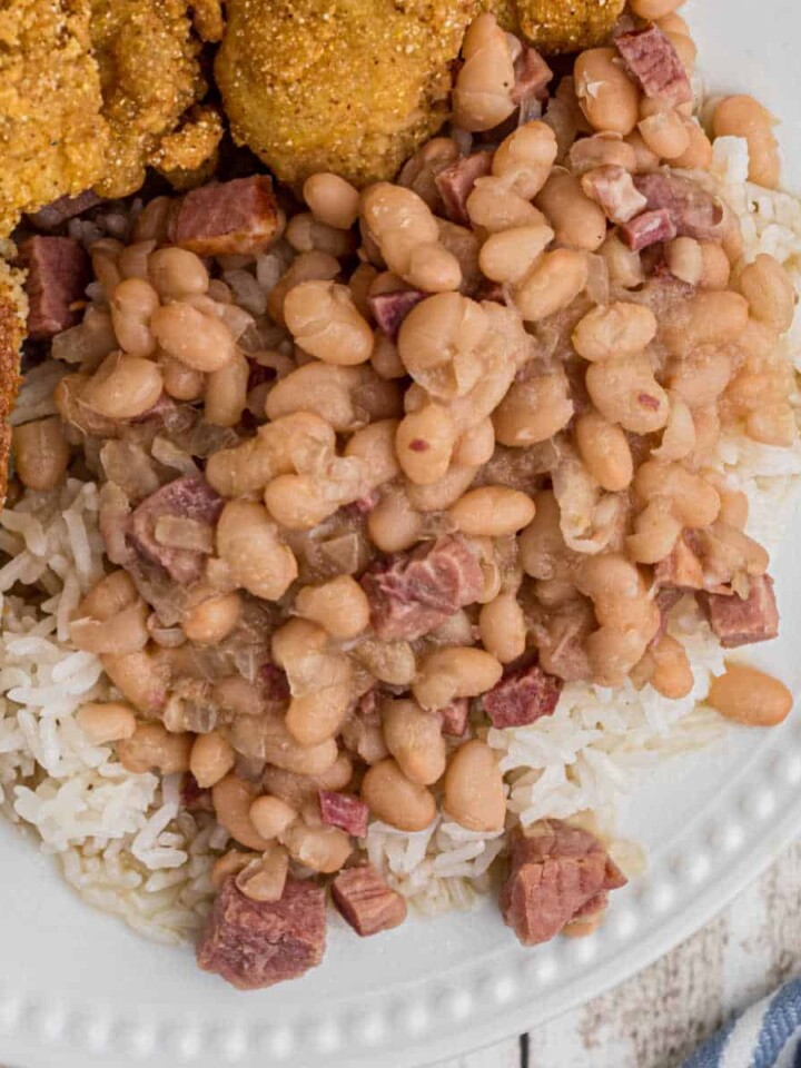 close up of white beans over rice on a plate with catfish peeking in