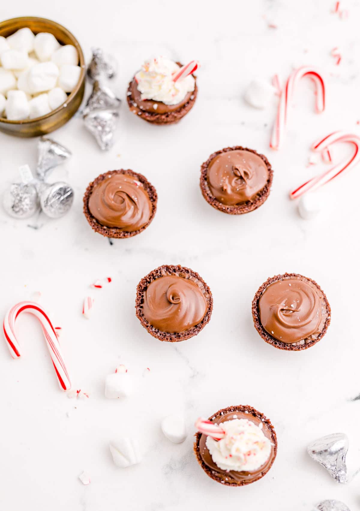 hot chocolate brownie bites laid out with a bowl of marshmallows and candy canes scattered around