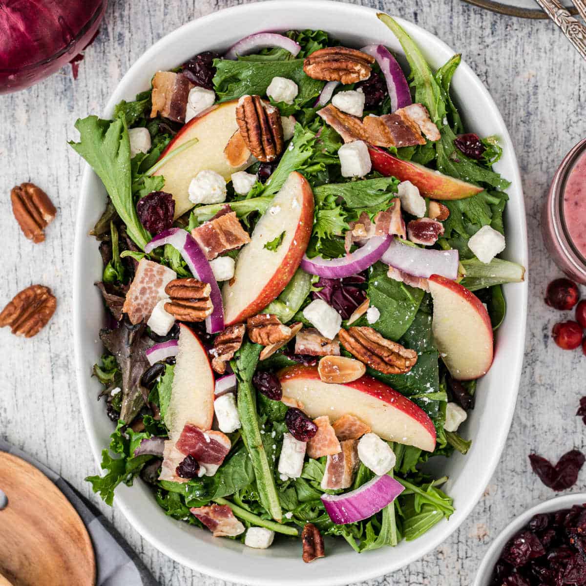 A bowl of salad with apples and red onions and cranberries with a spoon on the side