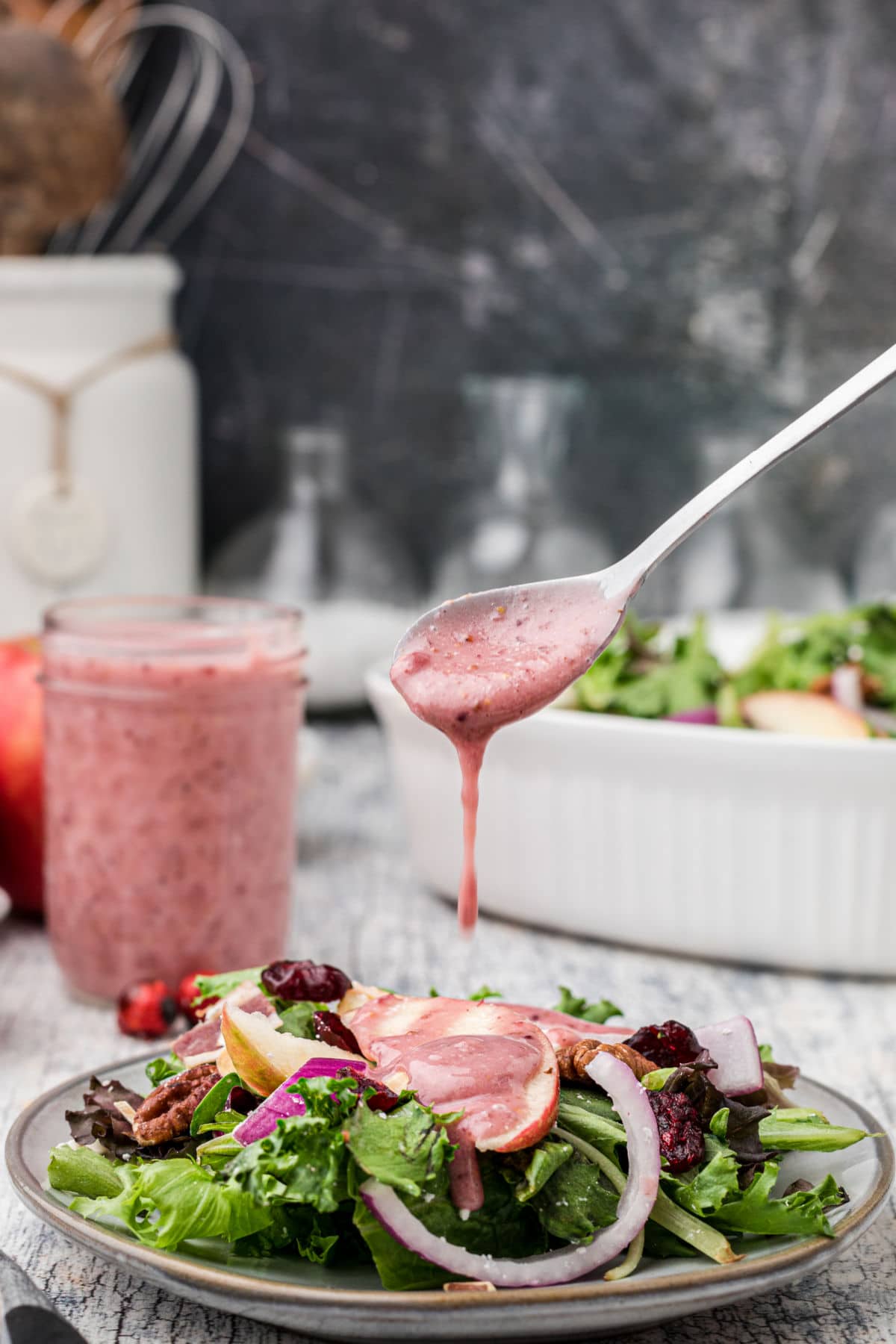 a spoon dripping cranberry vinaigrette all over a plate of salad