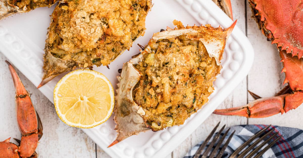 a stuffed crab shell with another behind it and a slice of lemon