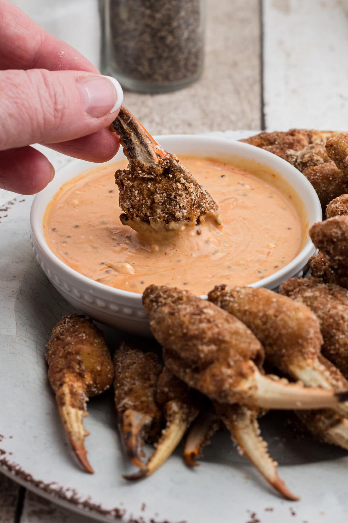 a fried crab claw being dipped into a pink sauce