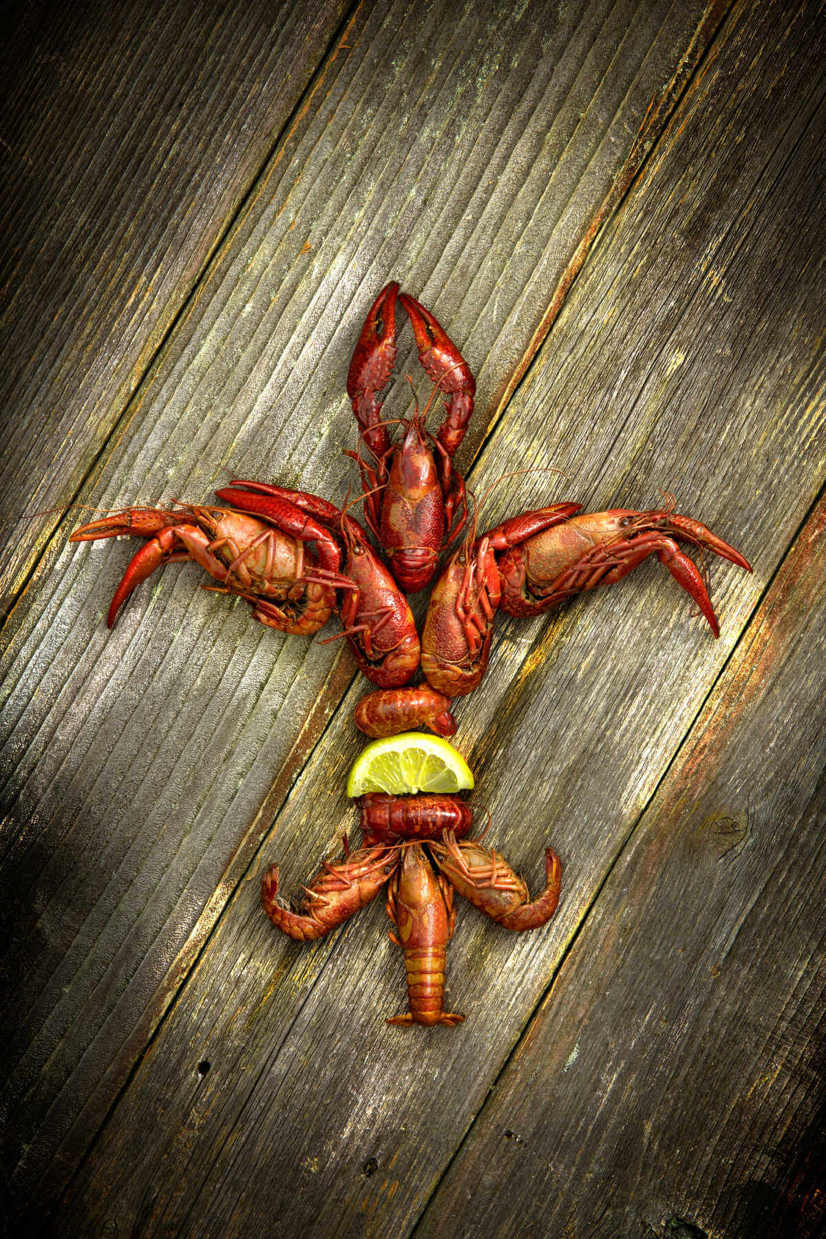 cooked crawfish laid out in a fleur de lis shape with a lemon, on a wooden distressed table