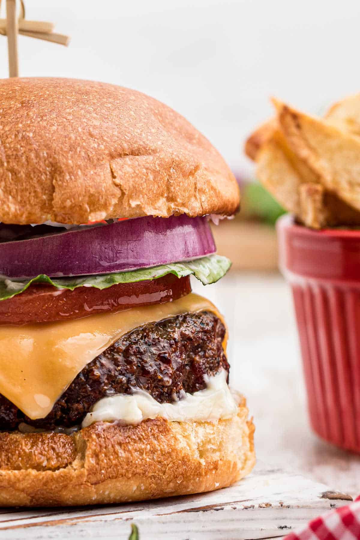 close up of a dressed venison burger with a bowl of french fries in the background