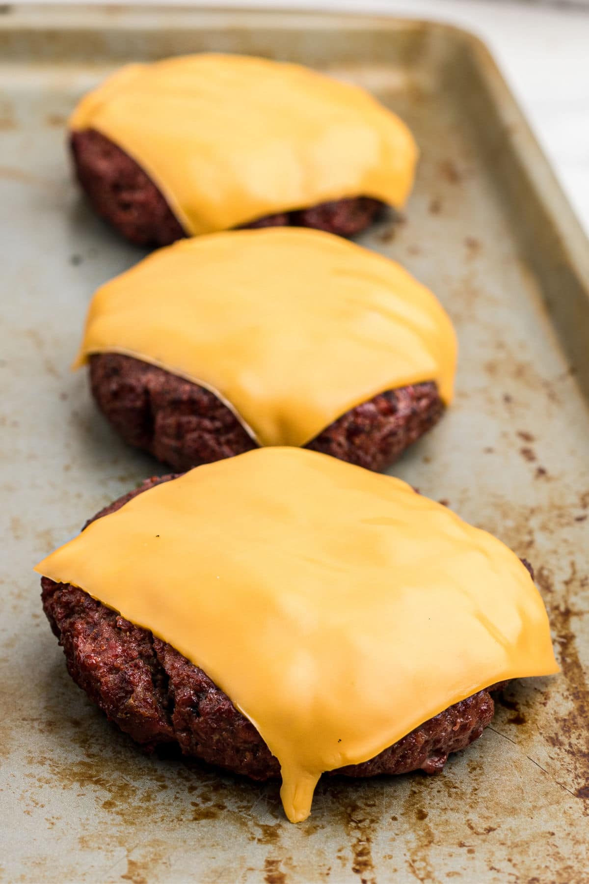 close up of some grilled venison burgers laid out with a slice of cheese on top