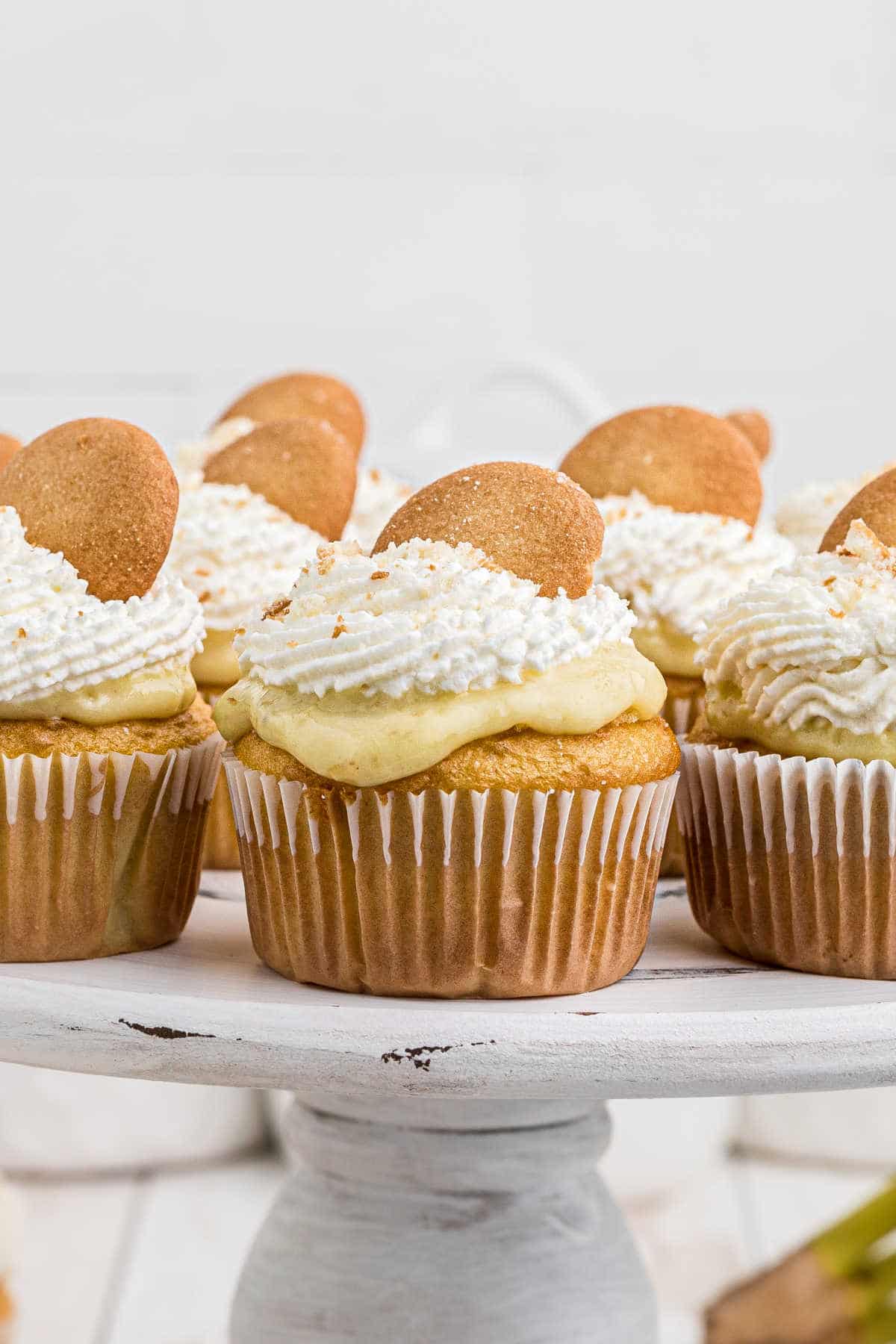 a cake stand filled with banana pudding cupcakes that have nilla wafers on top