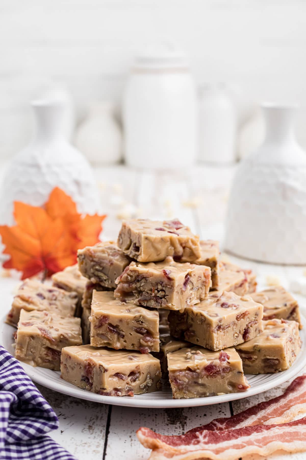 a plate full of maple bacon fudge with a maple leaf in the background and some bacon slices